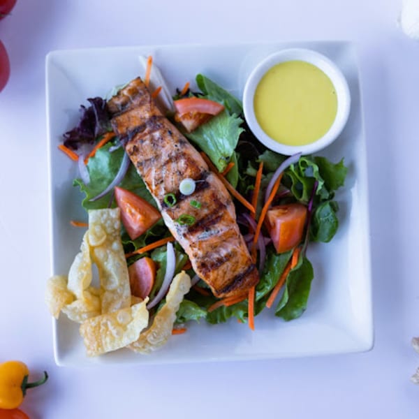 Grilled salmon salad with mixed greens, tomatoes, onions, crispy wontons, and a side of dressing.