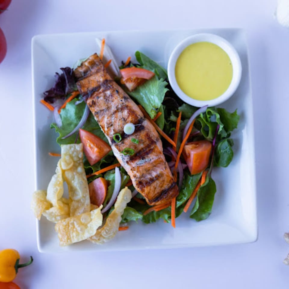 Grilled salmon salad with mixed greens, tomatoes, onions, crispy wontons, and a side of dressing.